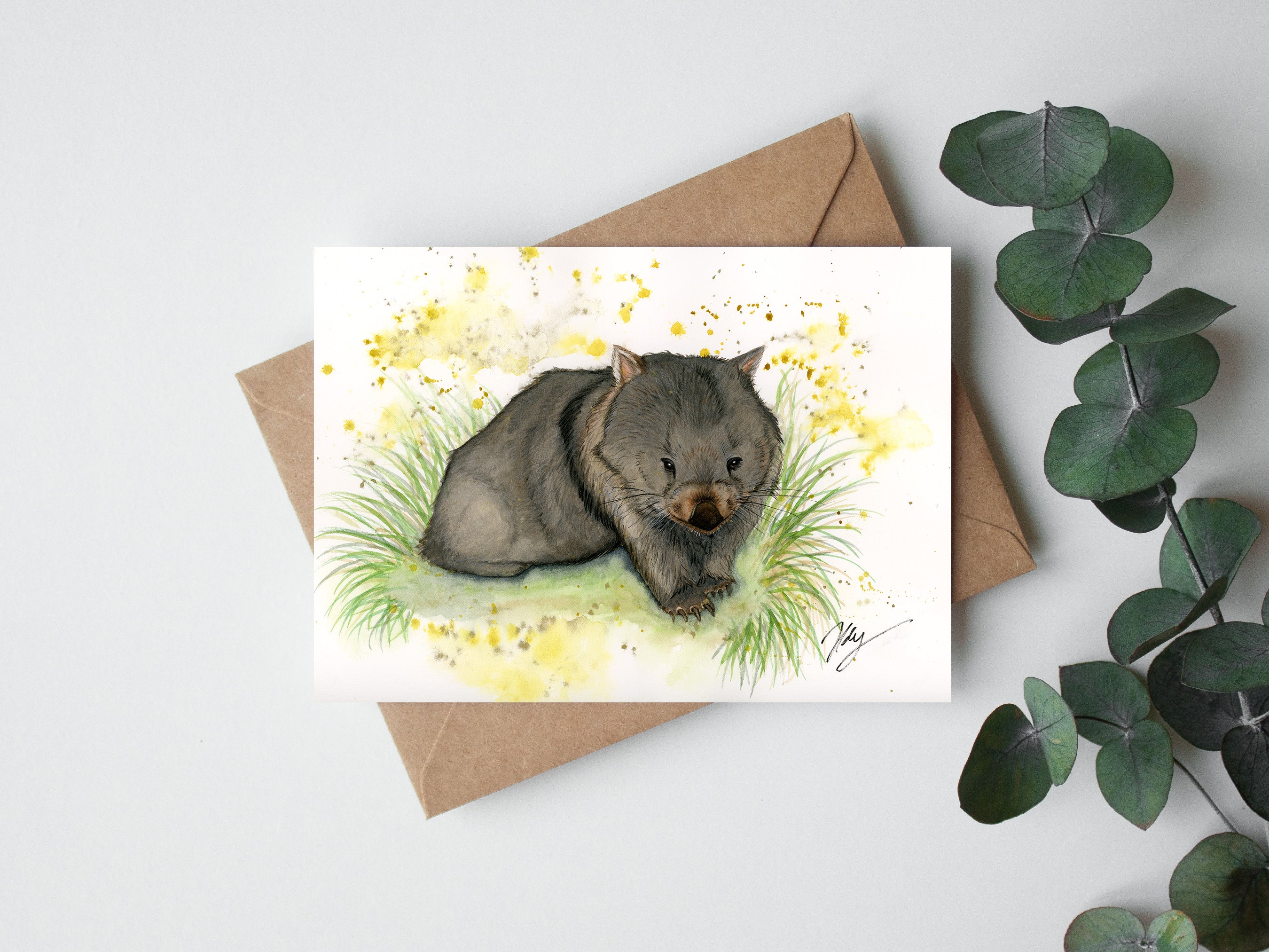 Card with a wombat illustration on a white background with a brown envelope and green leaves.
