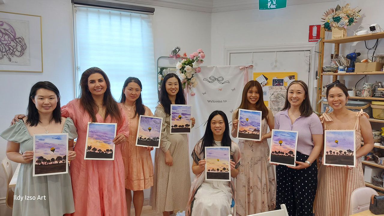 Group of women holding watercolour paintings in a workshop setting.